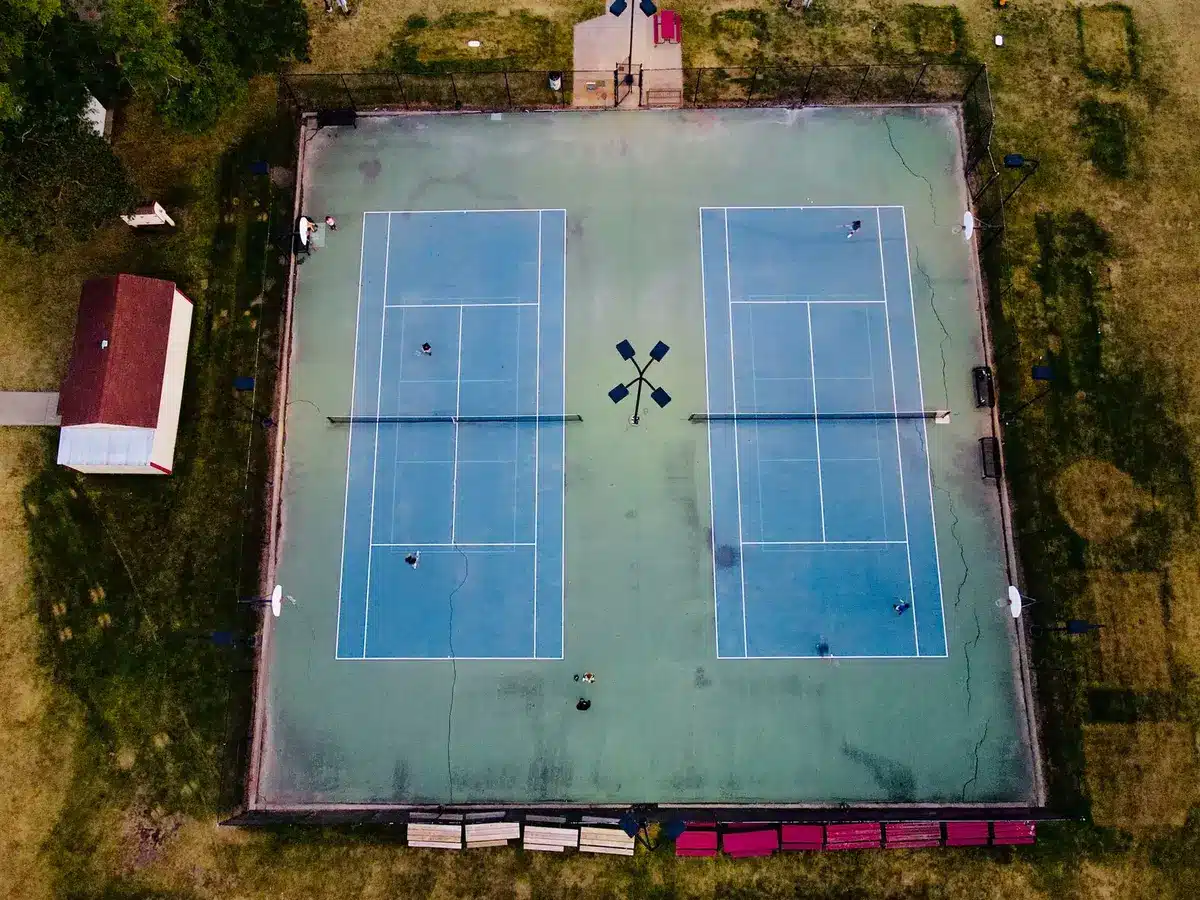 Tennisspelare i full sving på gräsbana under match med fullsatt stadion i bakgrunden