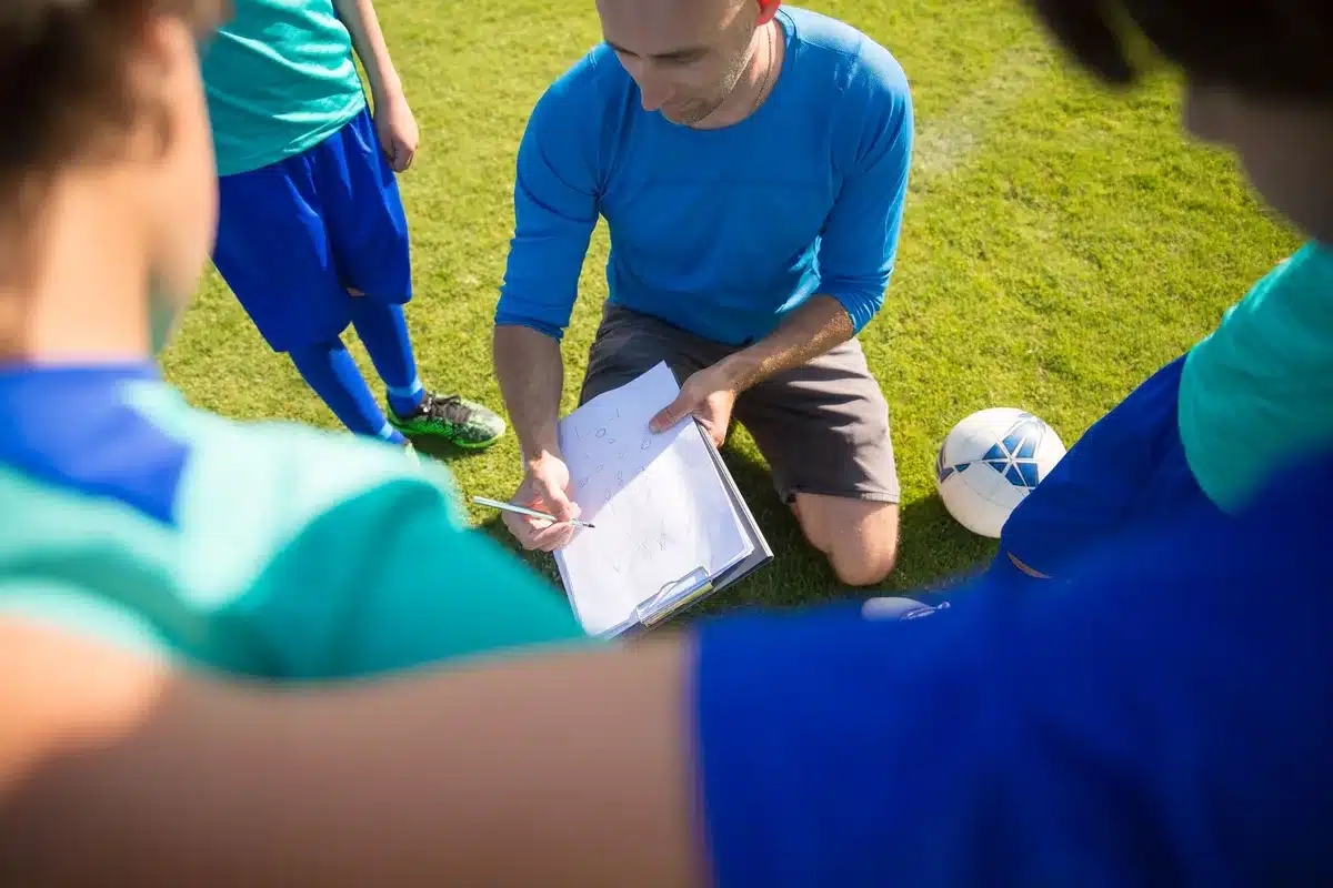 Fotbollstränare instruerar spelargrupp under träning på fotbollsplan
